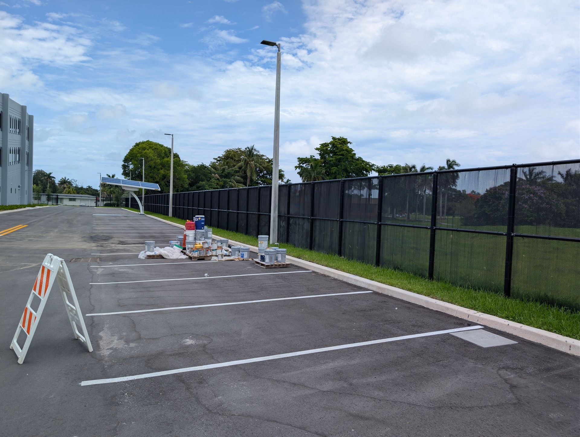 Empty parking lot with traffic cones and barricades beside a black fence on a cloudy day