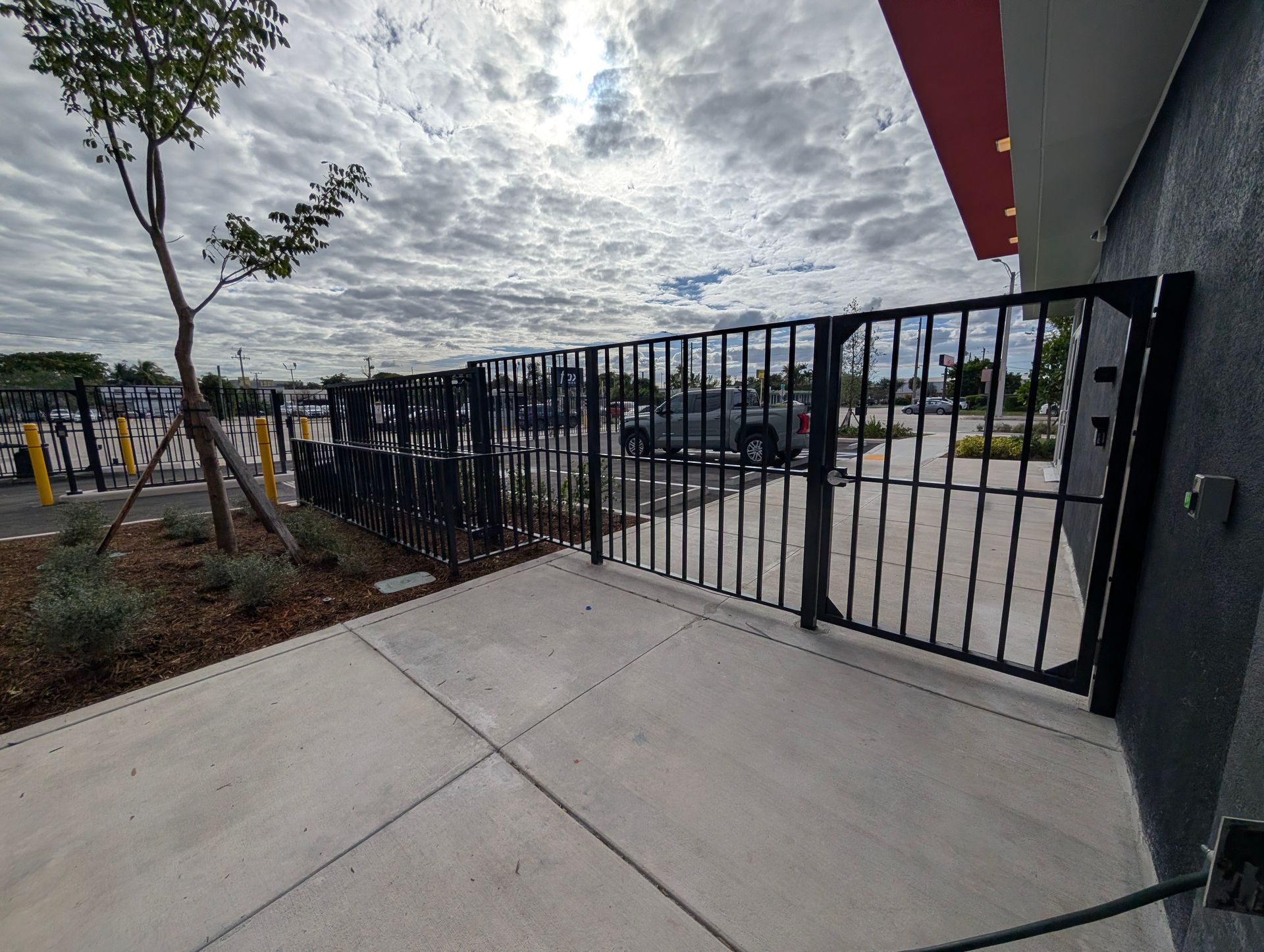 Gated sidewalk outside a building, with black metal fencing and a cloudy sky overhead.