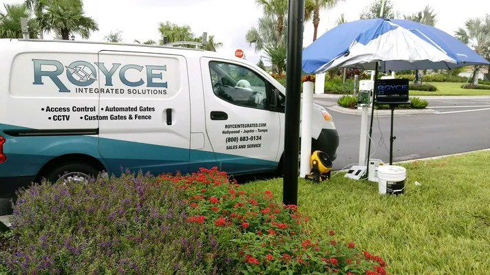 White Royce service van parked by a roadside tent with lawn equipment and flowering shrubs.