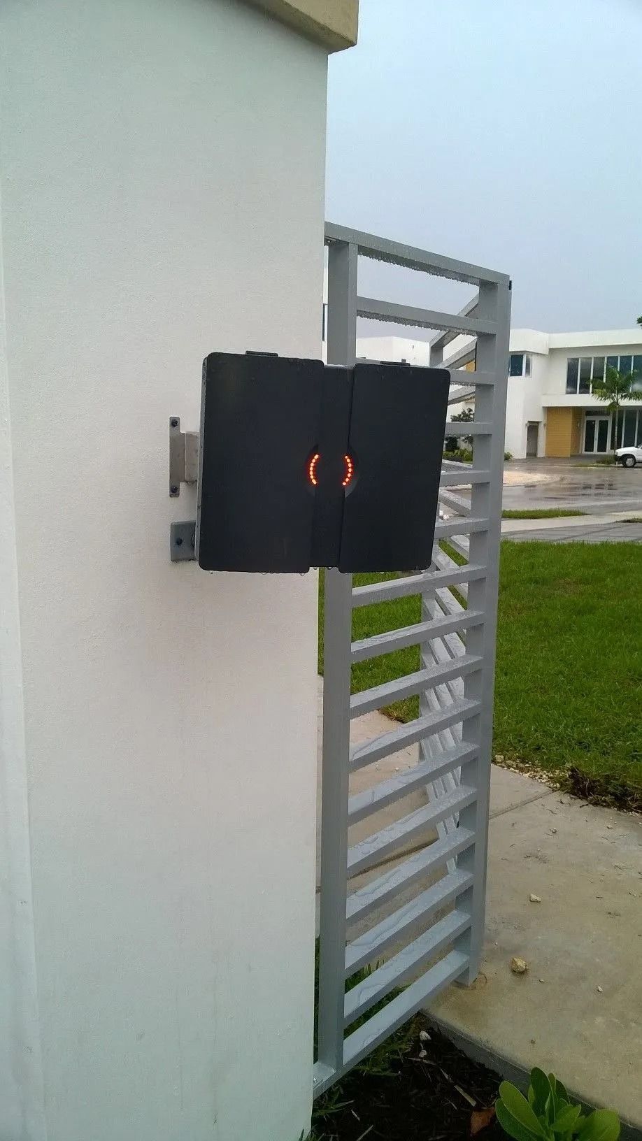 Black gate access panel mounted on a white wall beside a metal gate opening to a grassy yard