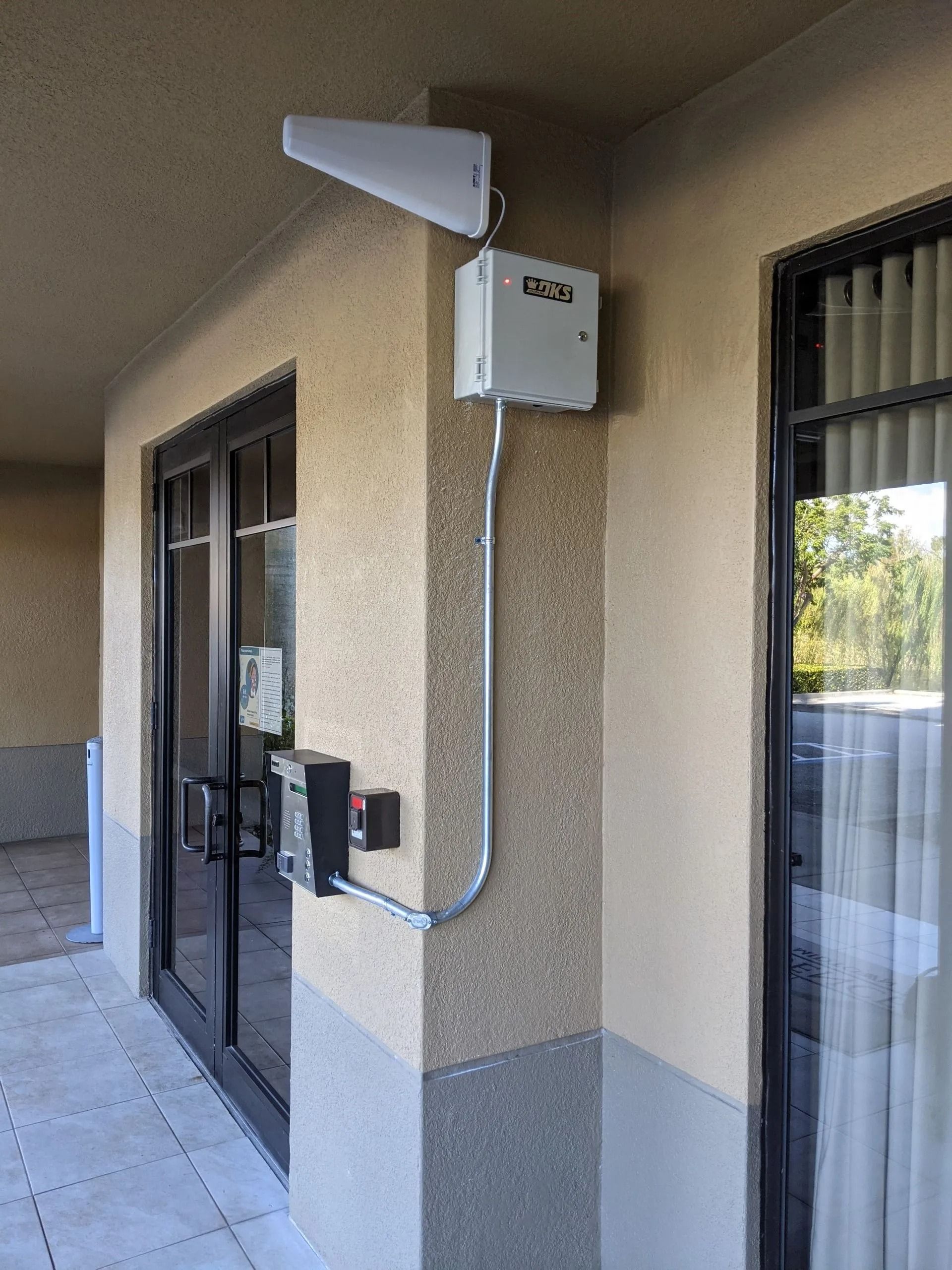 Apartment doorway with mounted security box, intercom, and white exterior speaker on a stucco wall