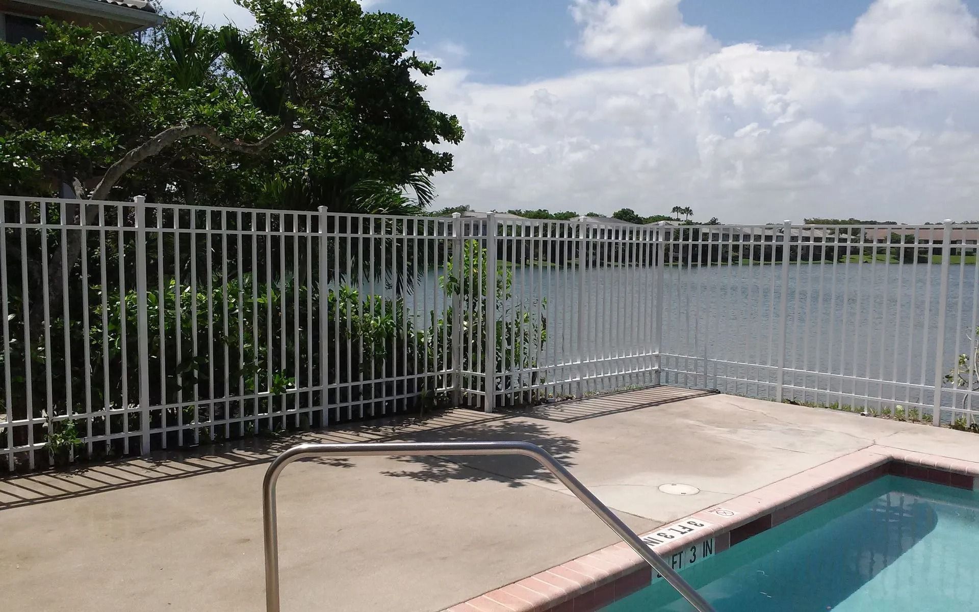 Swimming pool beside a metal fence and calm waterfront under cloudy skies