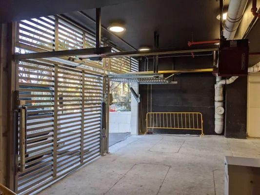 Covered parking area with metal slatted gates, concrete floor, and a yellow barrier in the background