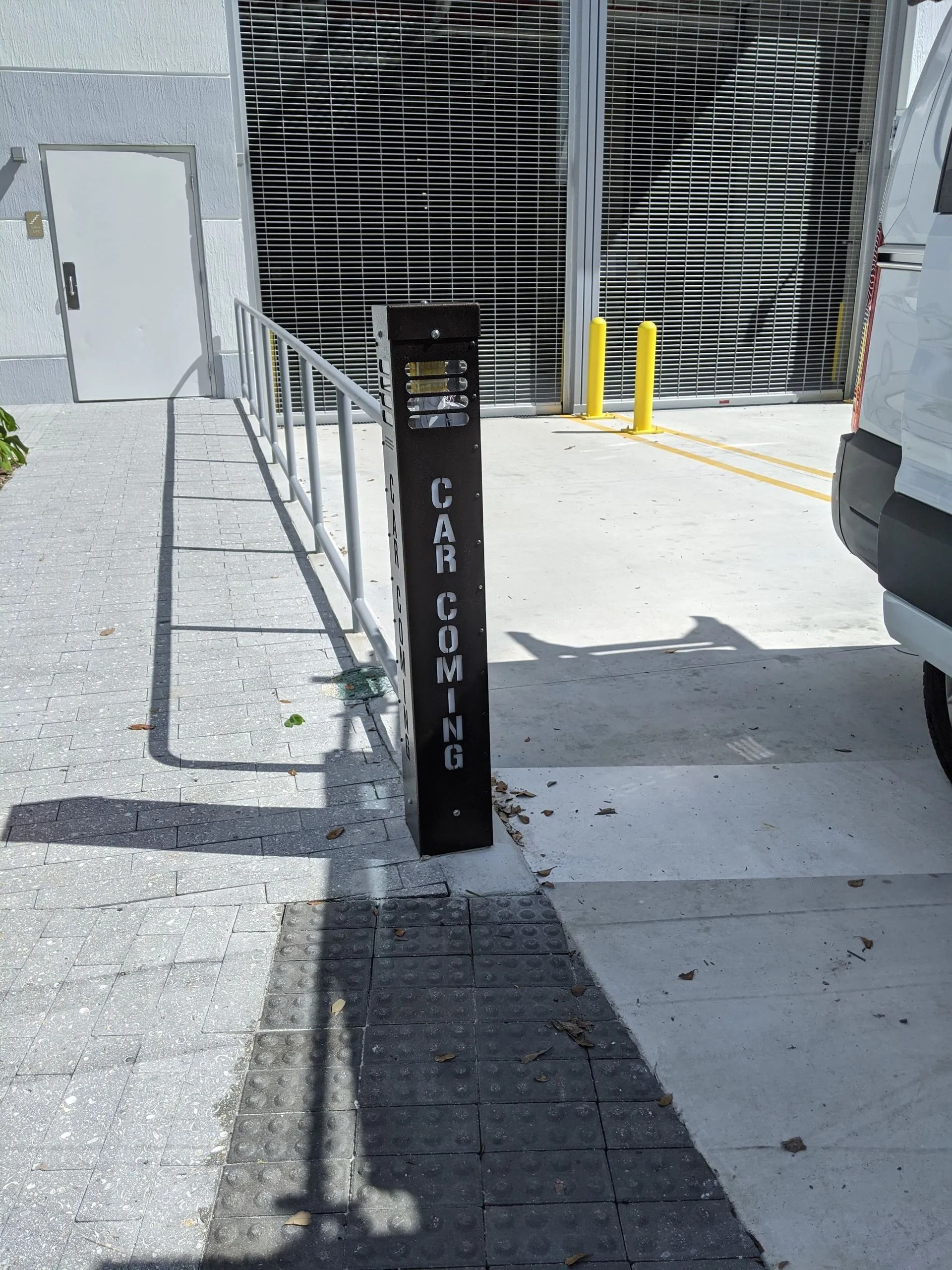 Black bollard labeled “AIR COMMAND” beside a bike rack and garage entrance in bright sunlight.