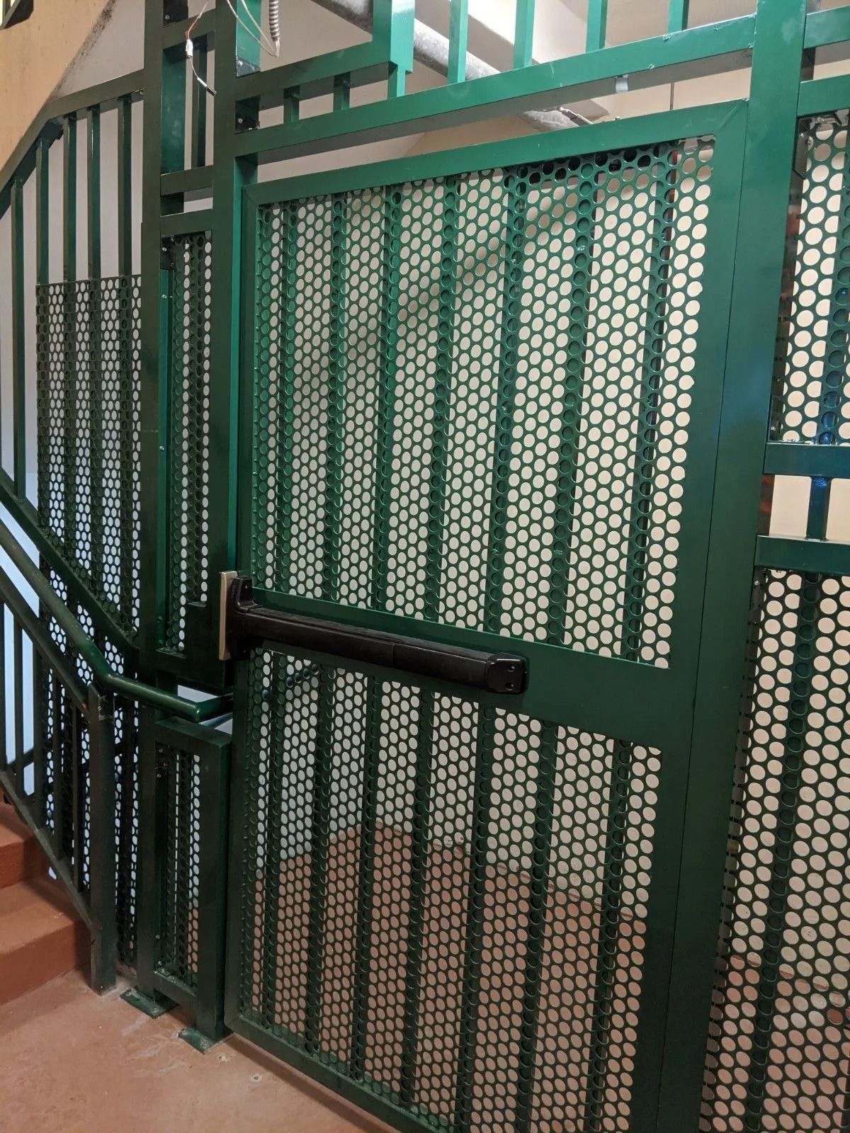 Green metal stair gate with mesh panels and a black handrail in an indoor stairwell