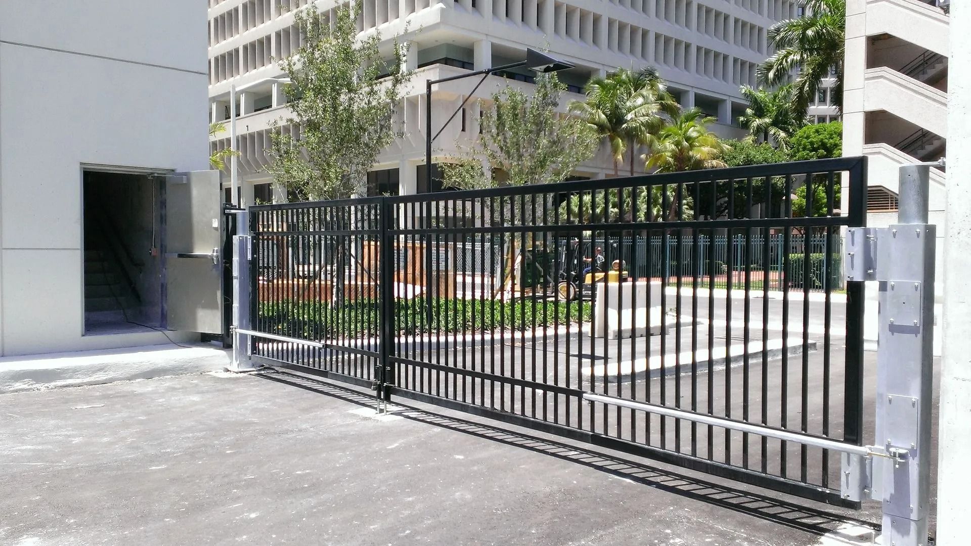 Black metal gate across a driveway beside a modern office building and landscaped courtyard.
