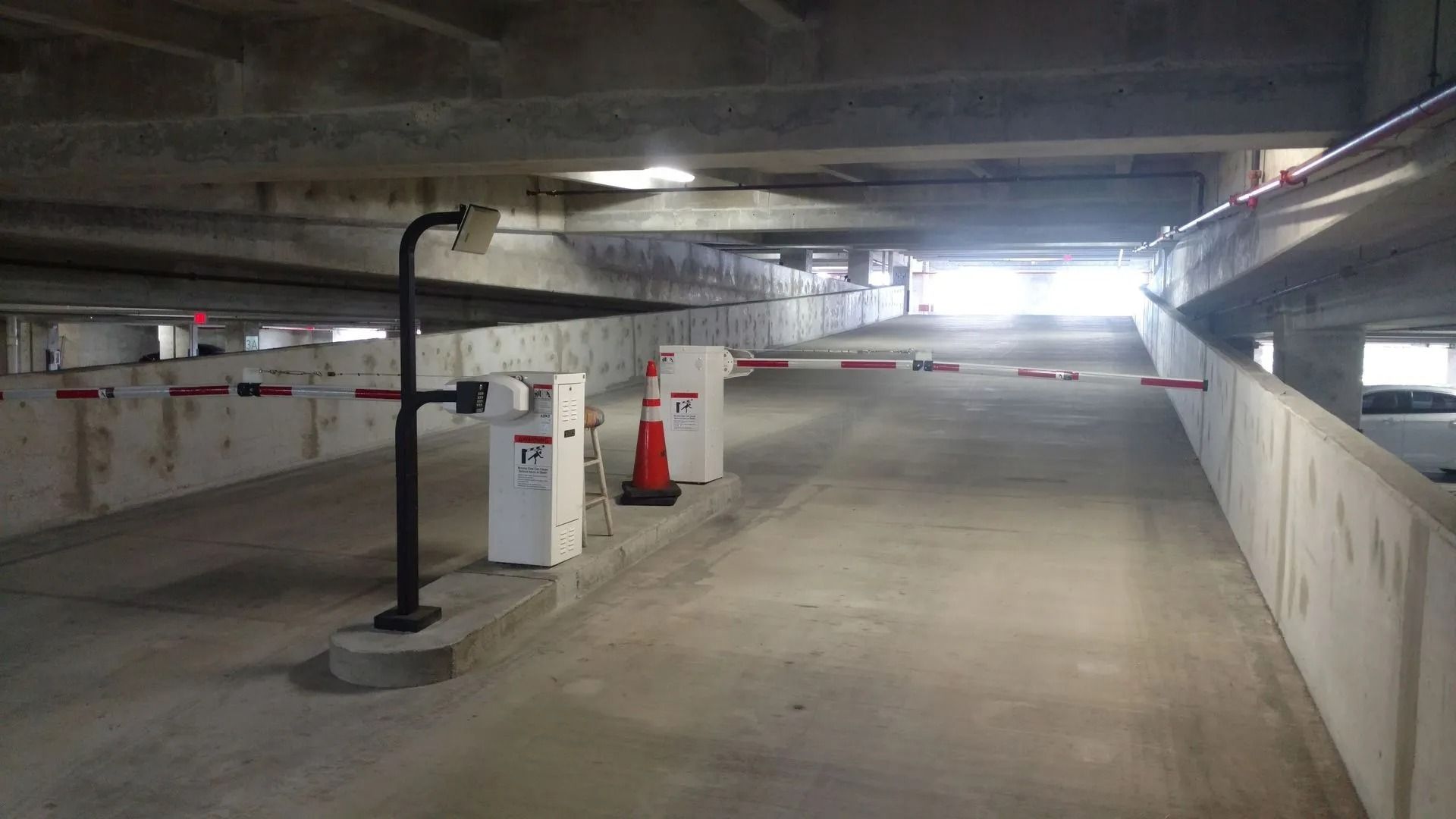 Empty underground parking garage with concrete ramps, pillars, and bright overhead lights.