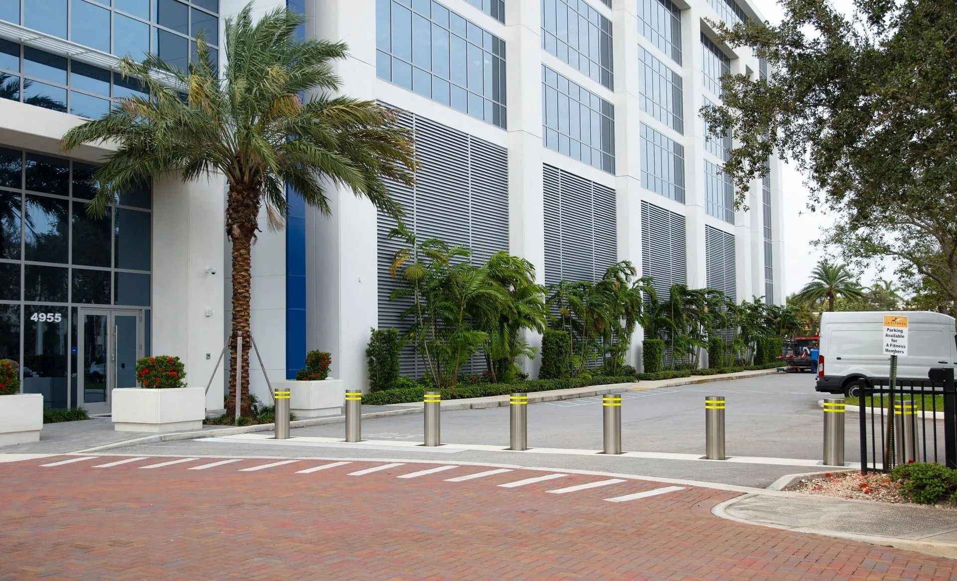 Modern office building entrance with palm trees, yellow bollards, and a white truck parked nearby