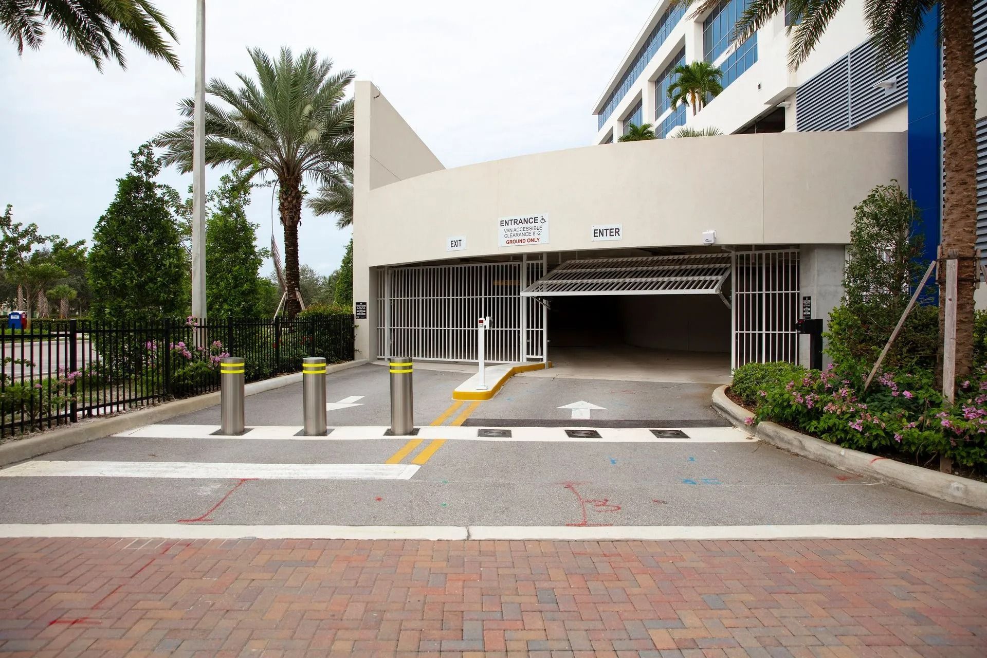 Modern building entrance with palm trees, bollards, and a covered driveway at the curb.