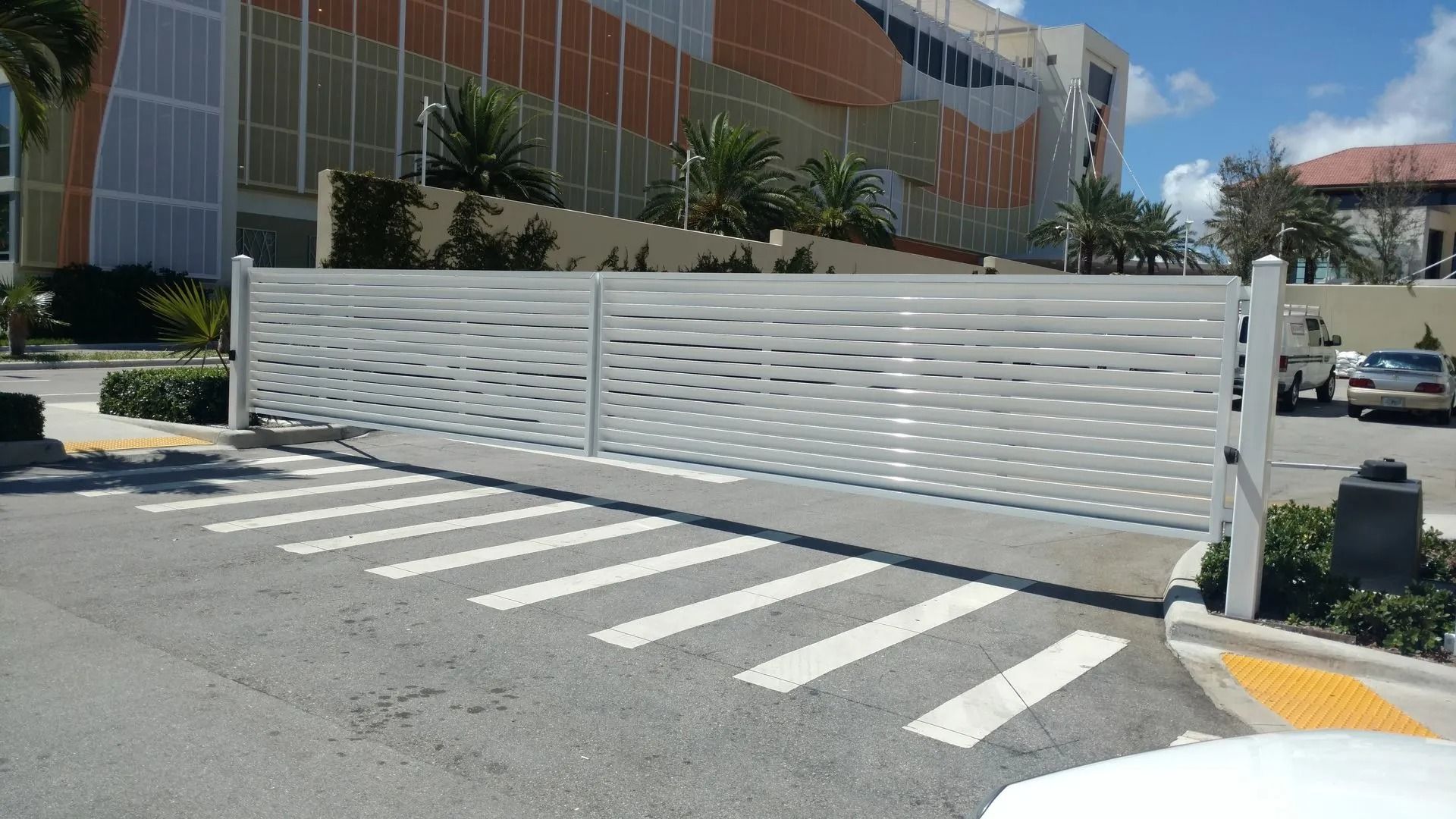 White fence across a crosswalk in front of a modern building on a sunny day
