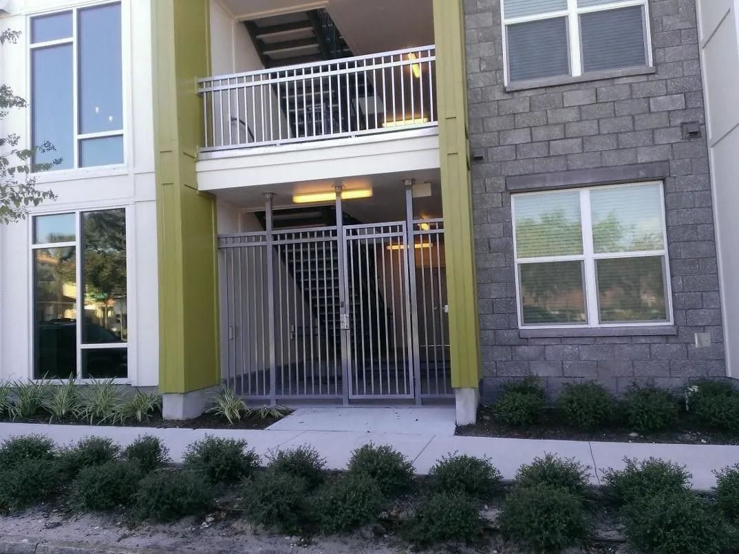 Apartment building entrance with green siding, white balconies, and a metal security gate.