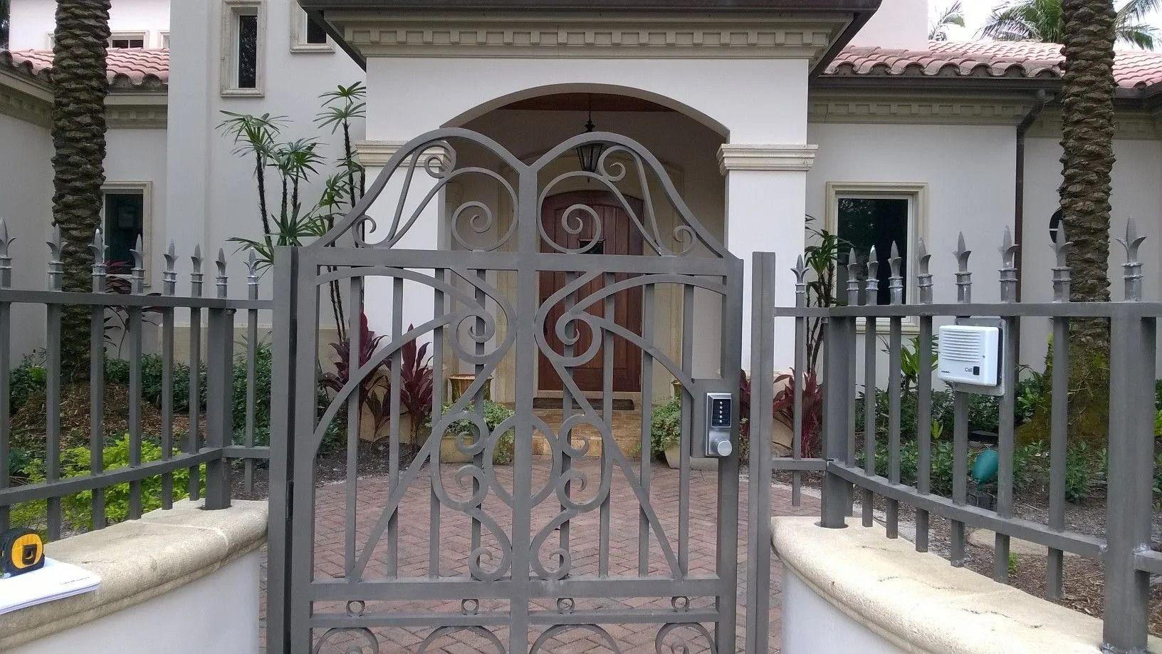 Gated entrance to a white house with arched porch, iron fence, and brick walkway
