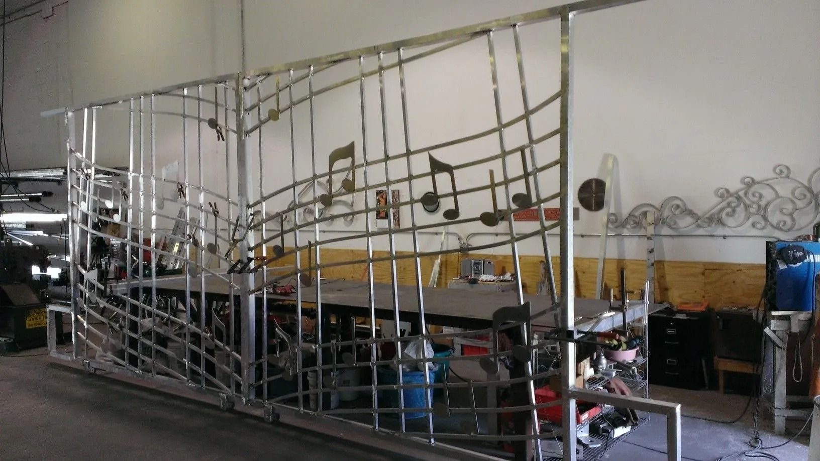 A metal framework surrounds a cluttered workshop area with tools, tables, and equipment.