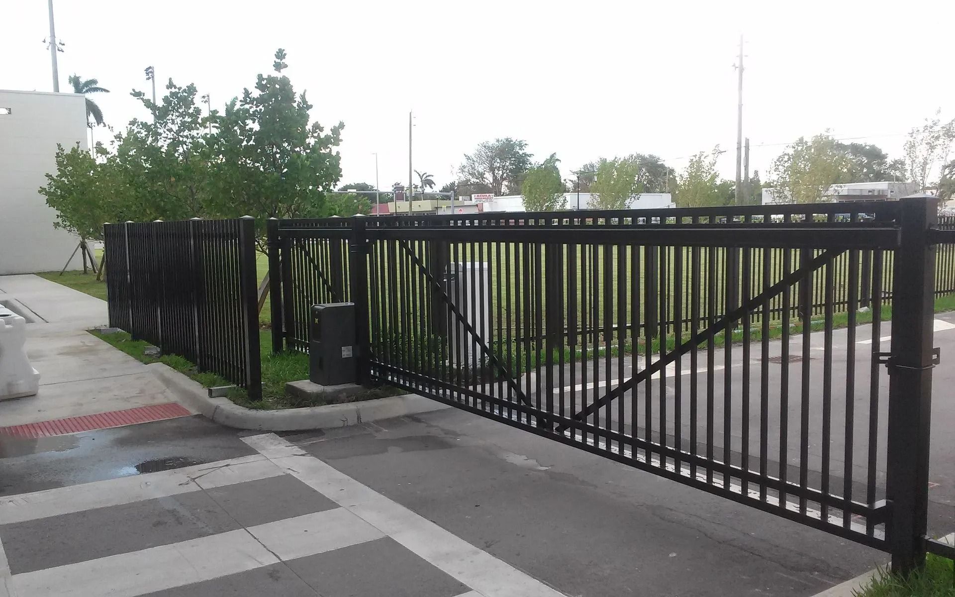 Black metal sliding gate across a driveway beside a sidewalk and trees
