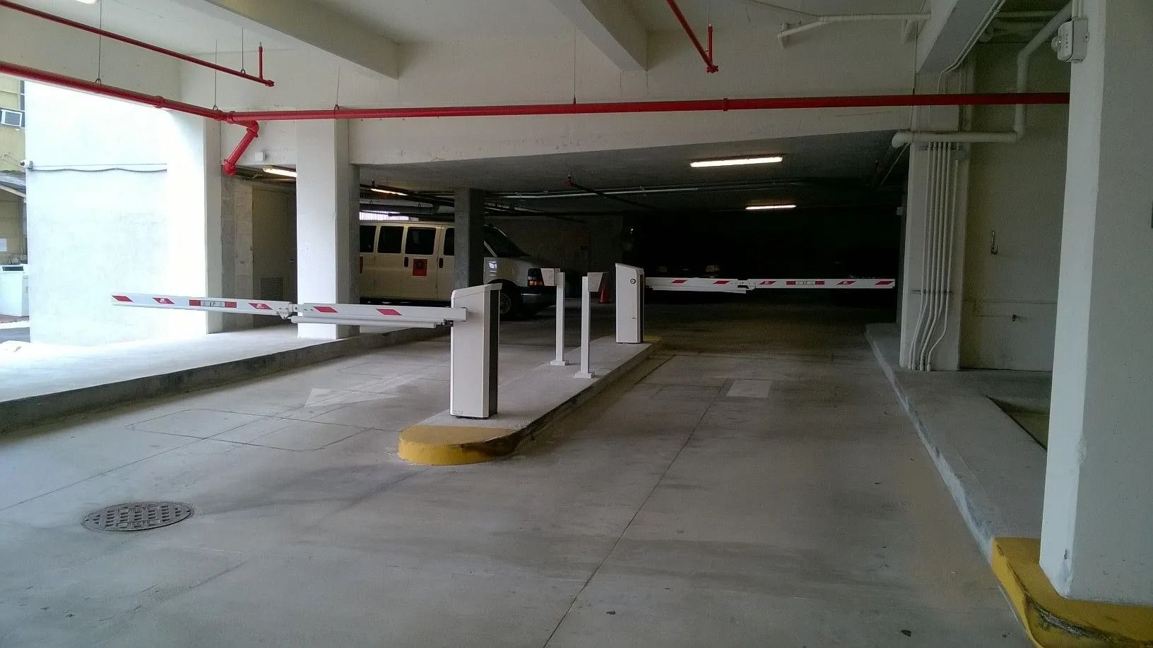 Empty parking garage with concrete pillars, a low ceiling, and a dim ramp leading into darkness