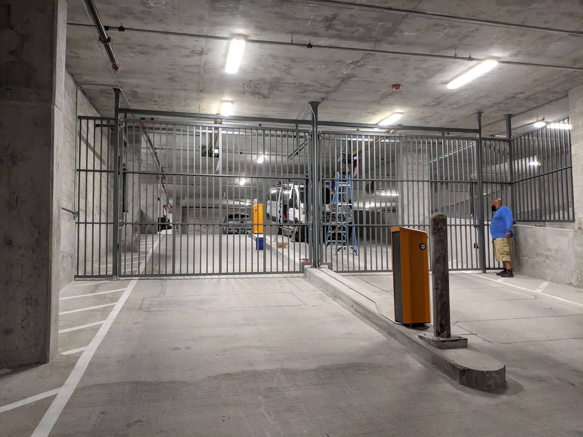 Concrete parking garage entrance with metal security gates and two workers nearby