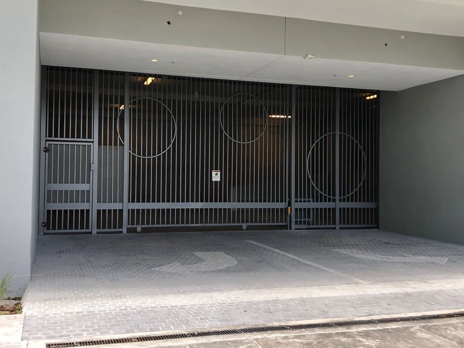Gray metal security gate across a covered garage entrance with concrete driveway.