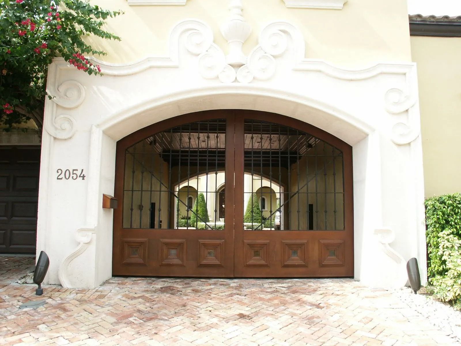 White stucco garage with arched wooden double doors and a house number on the left side.
