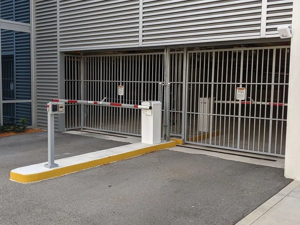 White security gate barrier at a building entrance with a closed metal gate and yellow curb stop.