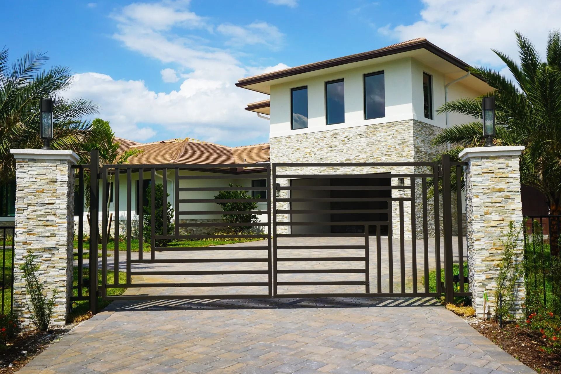 Modern house with stone pillars and black metal gate under a blue sky