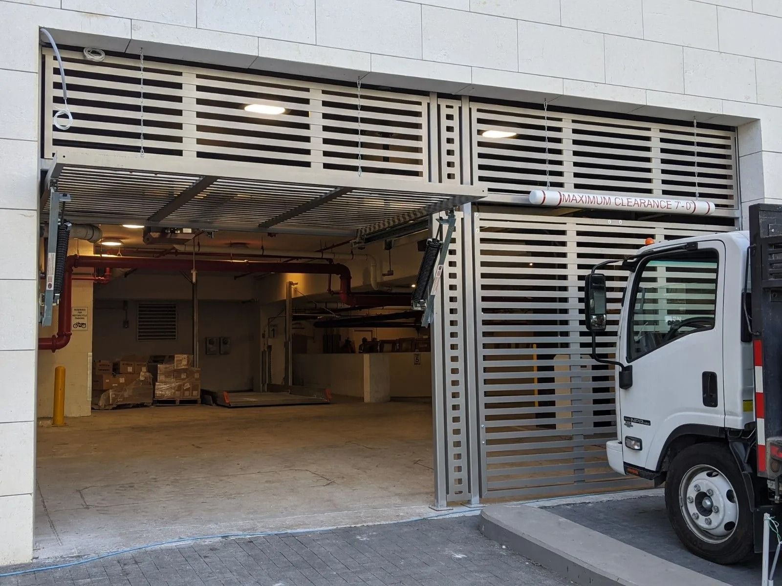 Open garage with metal louvered doors and a white truck parked at the entrance
