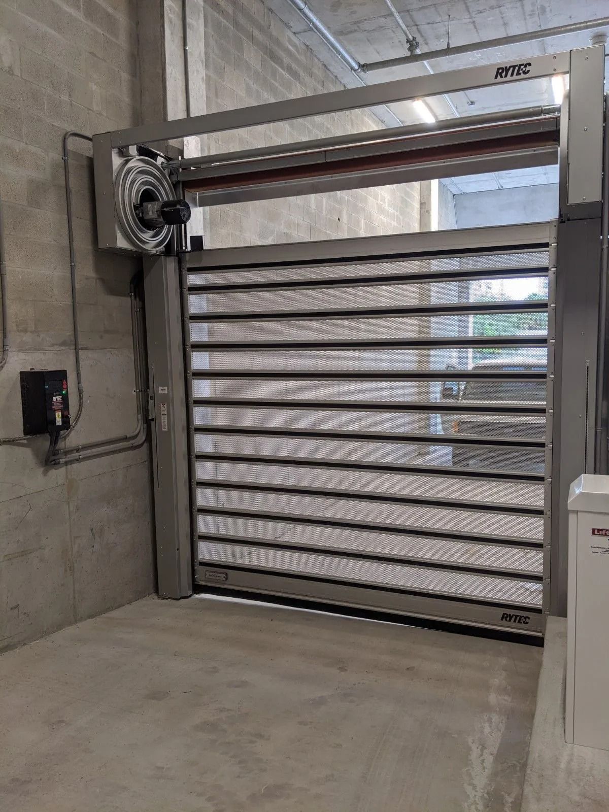 Industrial roll-up shutter with horizontal slats in a concrete garage or loading bay.