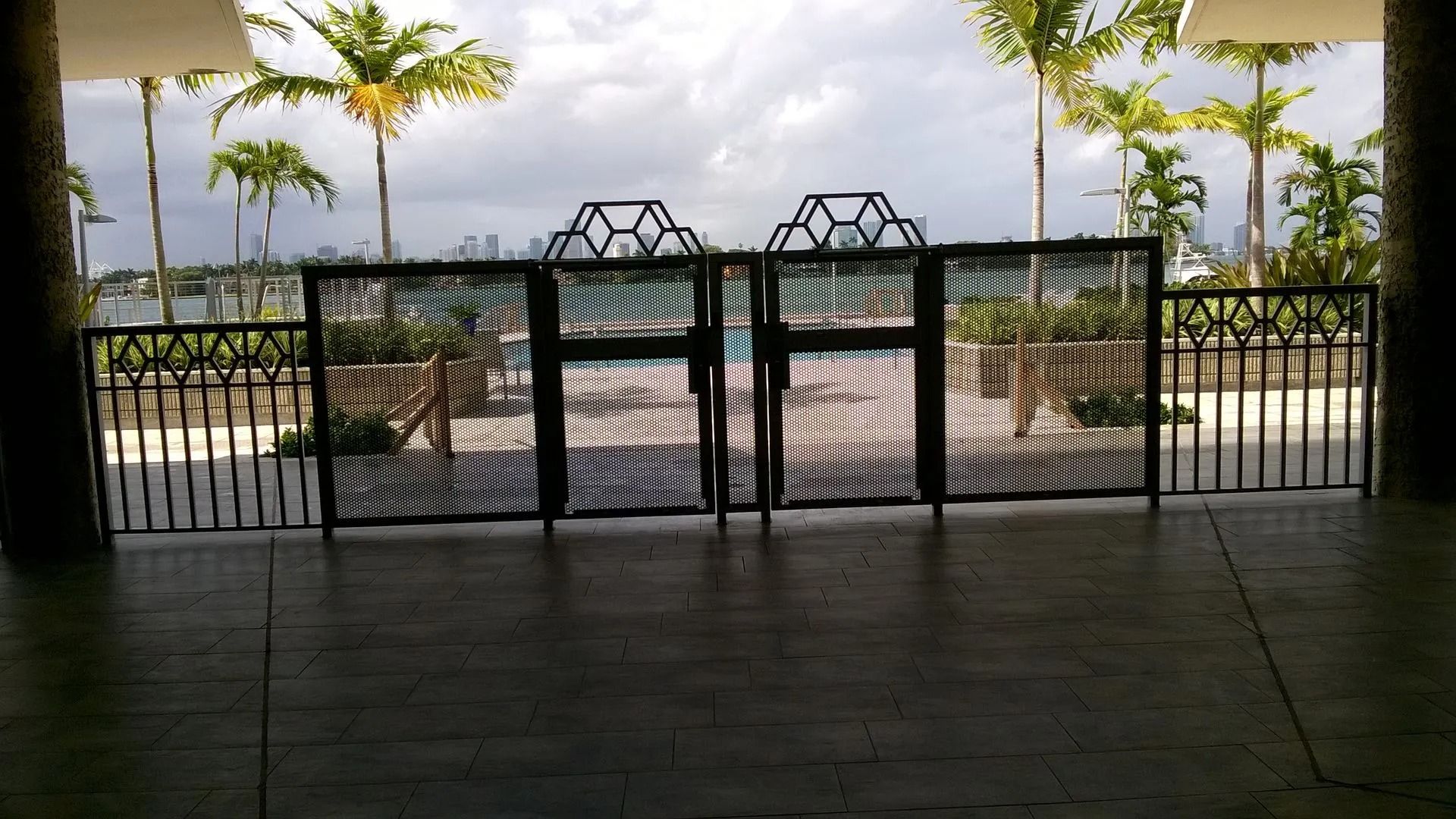 Open gate to a poolside patio with palm trees and a bright view beyond
