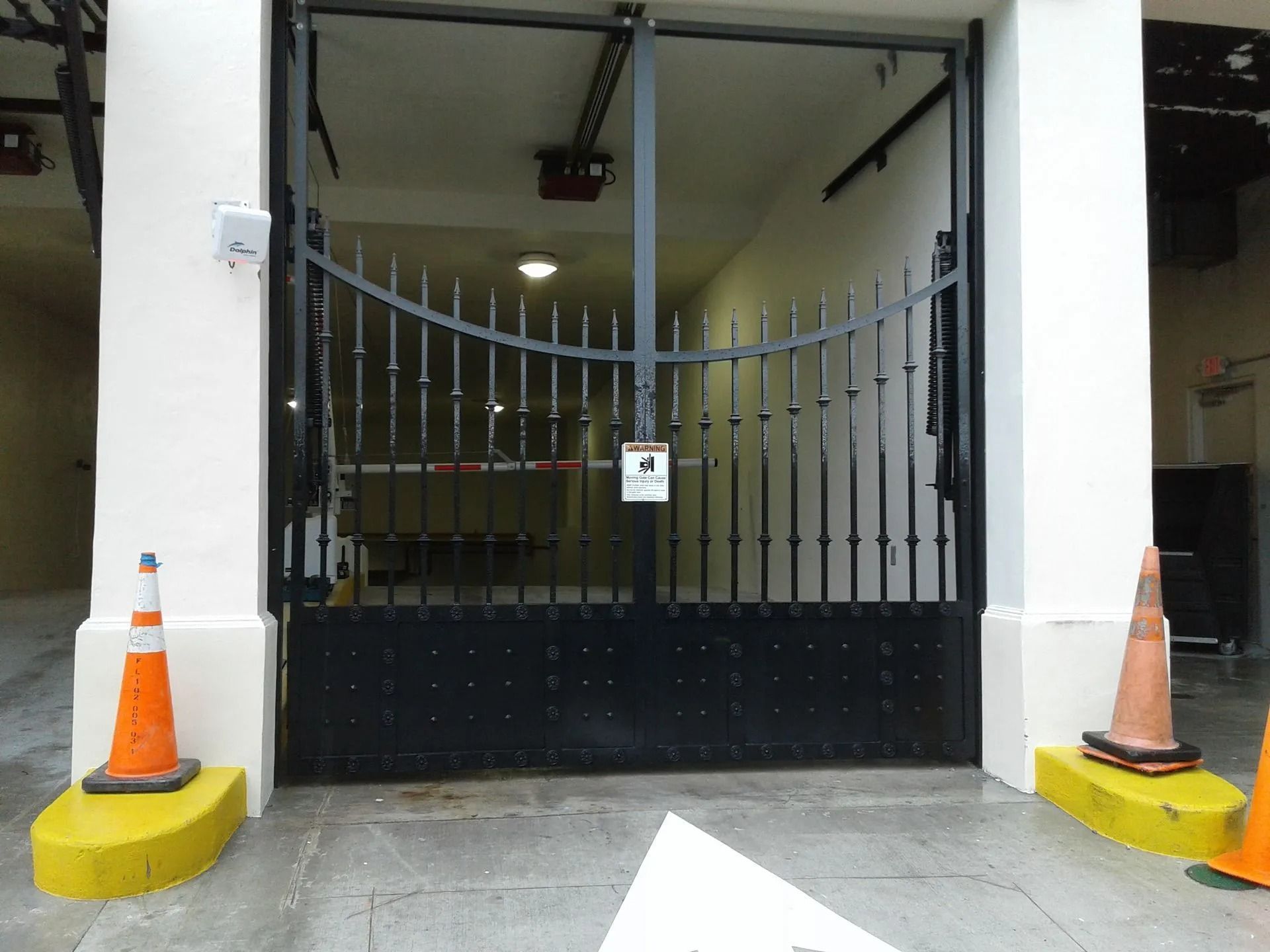 Gated building entrance with black metal gate, orange cones, and yellow curb markers