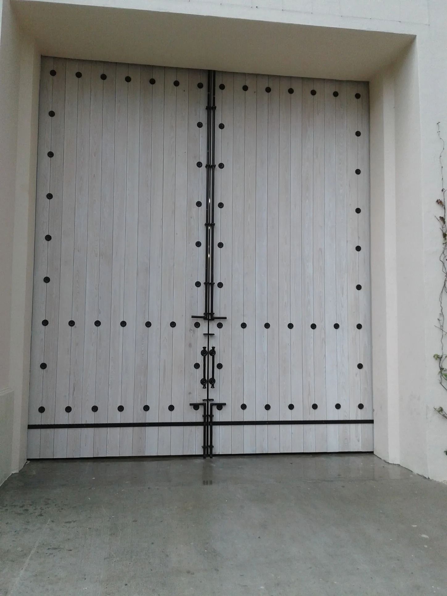 Closed white double wooden doors with a central metal latch in a plain stucco entryway
