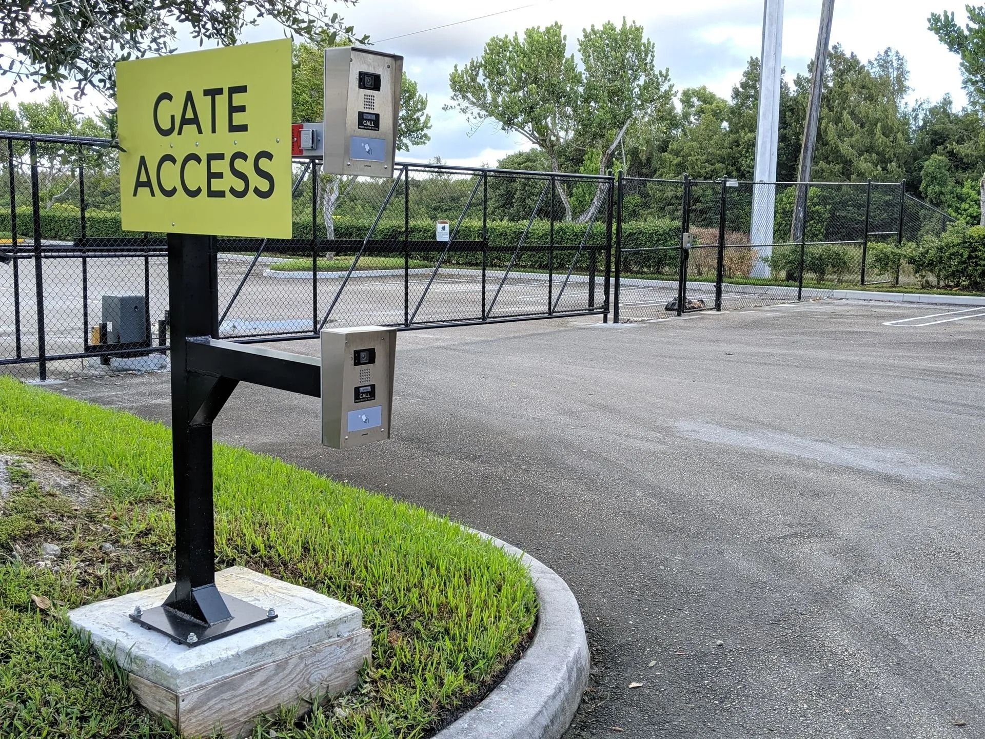 Gate access sign beside a closed driveway barrier at an industrial lot entrance