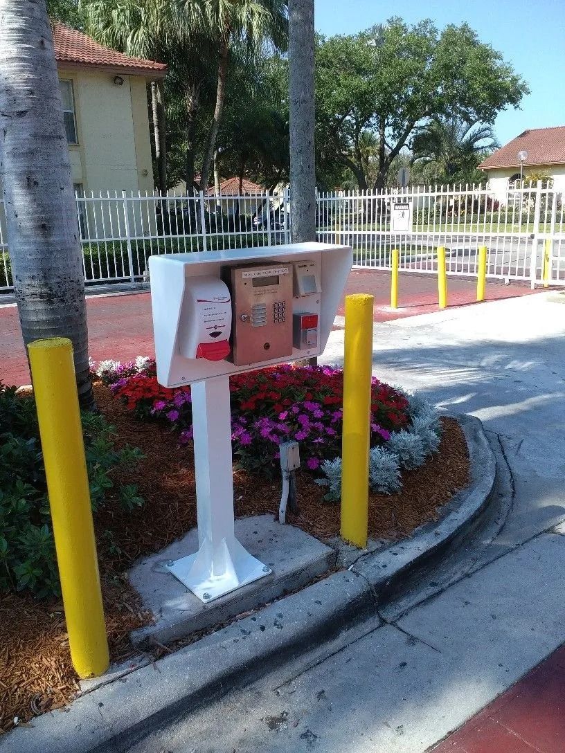 Outdoor utility box beside a driveway, surrounded by flowers and yellow bollards.