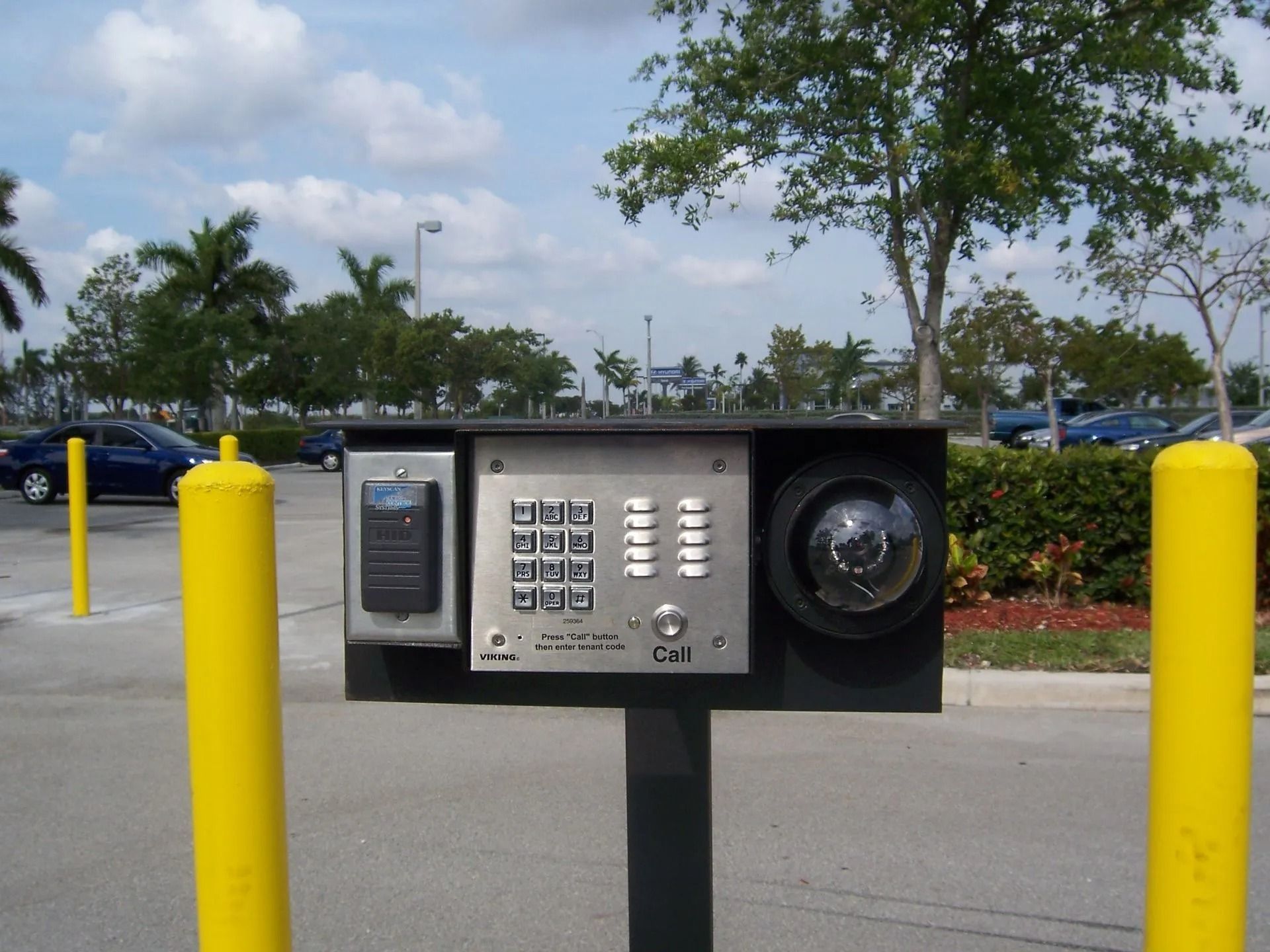 Outdoor emergency phone and keypad station on a parking lot island with yellow bollards