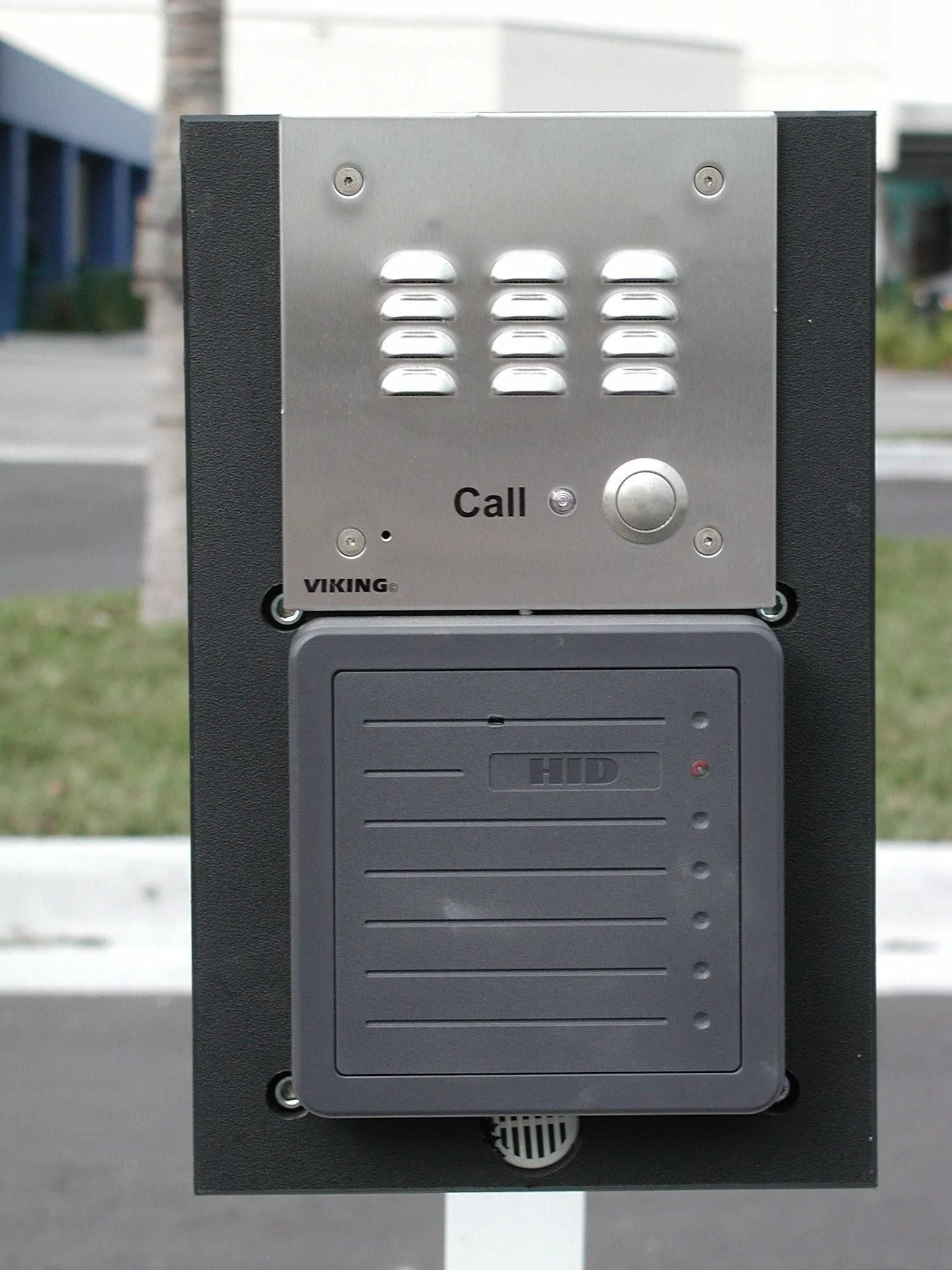 Outdoor intercom call panel with speaker grille and round button mounted on a black post
