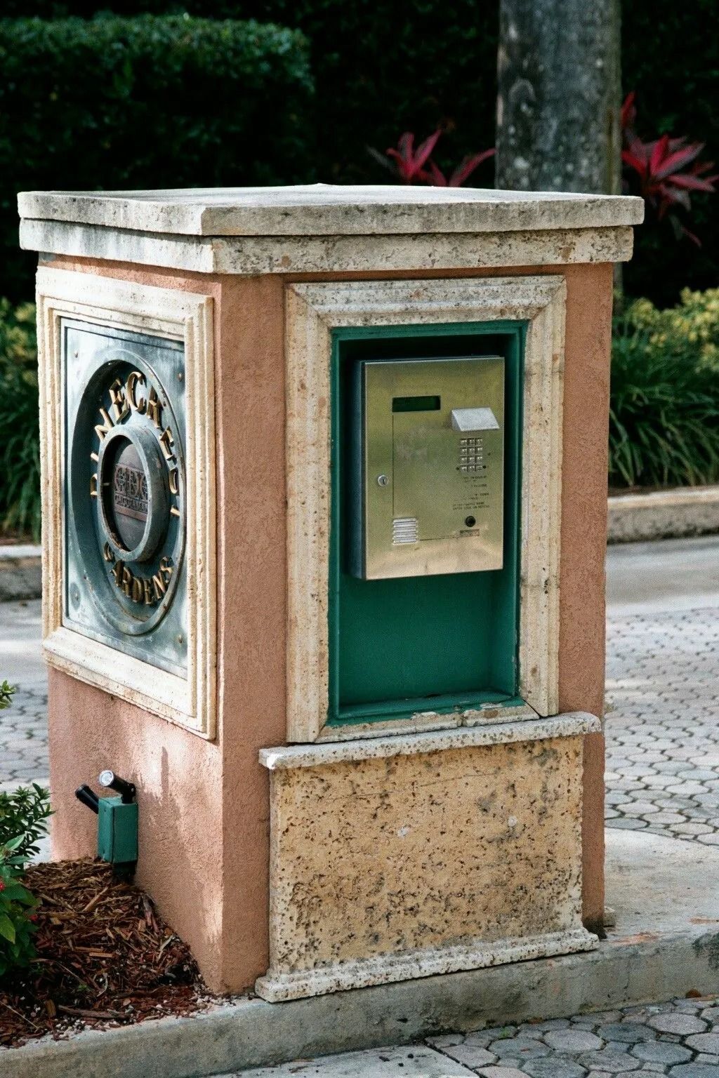 Stone utility pedestal with a green panel and circular metal fixture beside a sidewalk