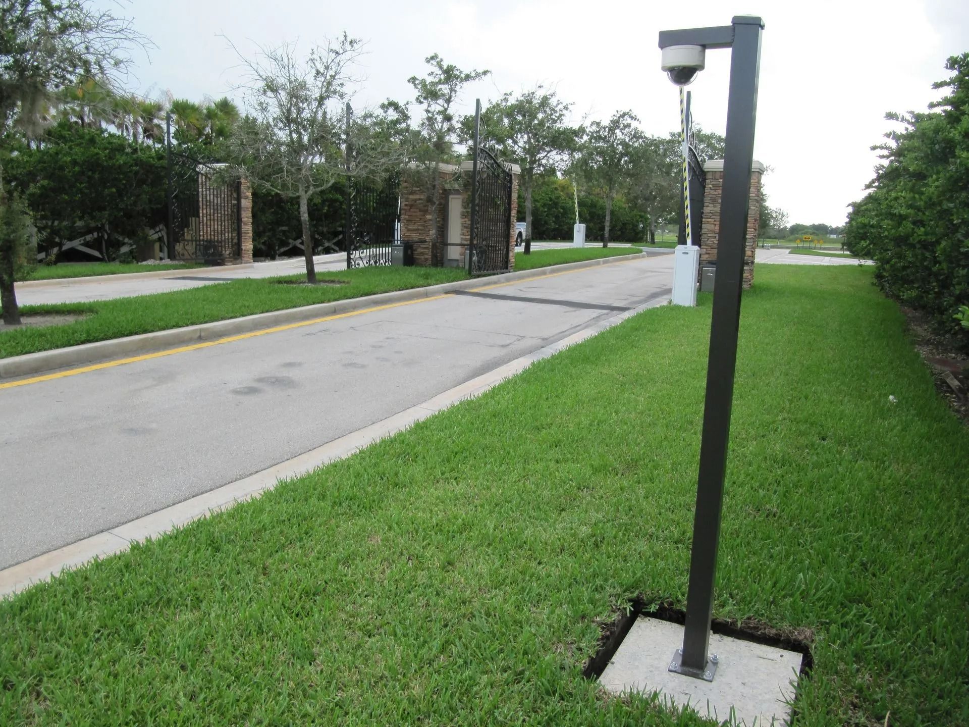 Roadside black lamp post beside a grassy sidewalk and quiet street with trees in the background