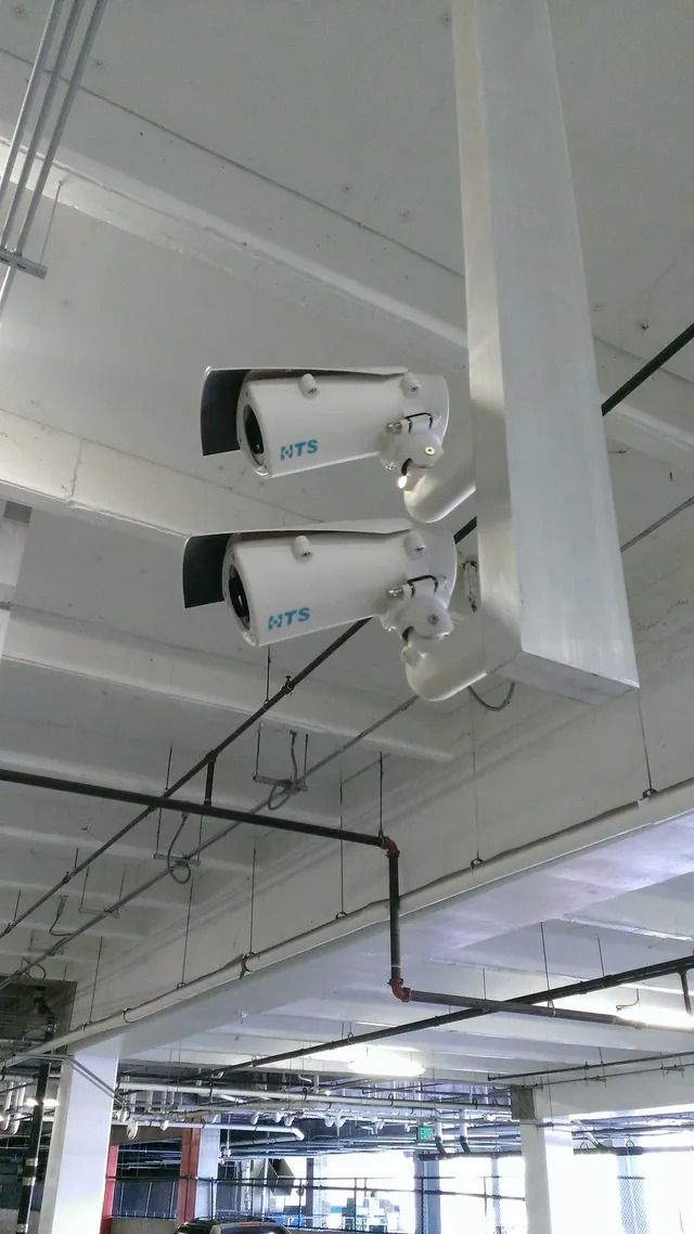 Two white security cameras mounted on a concrete ceiling in a parking garage