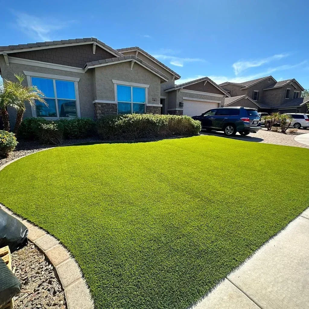 A house with a vibrant green lawn, blue windows, and a car parked in front on a sunny day.