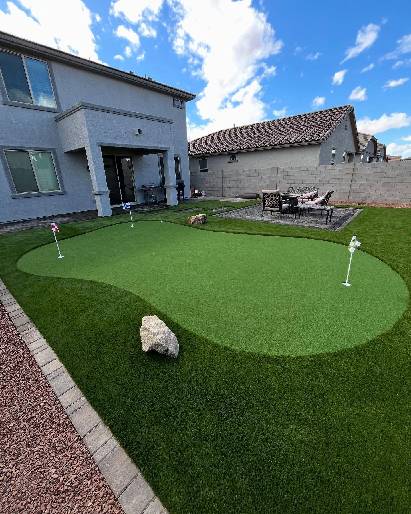 Backyard with putting green, house in background, clear blue sky.