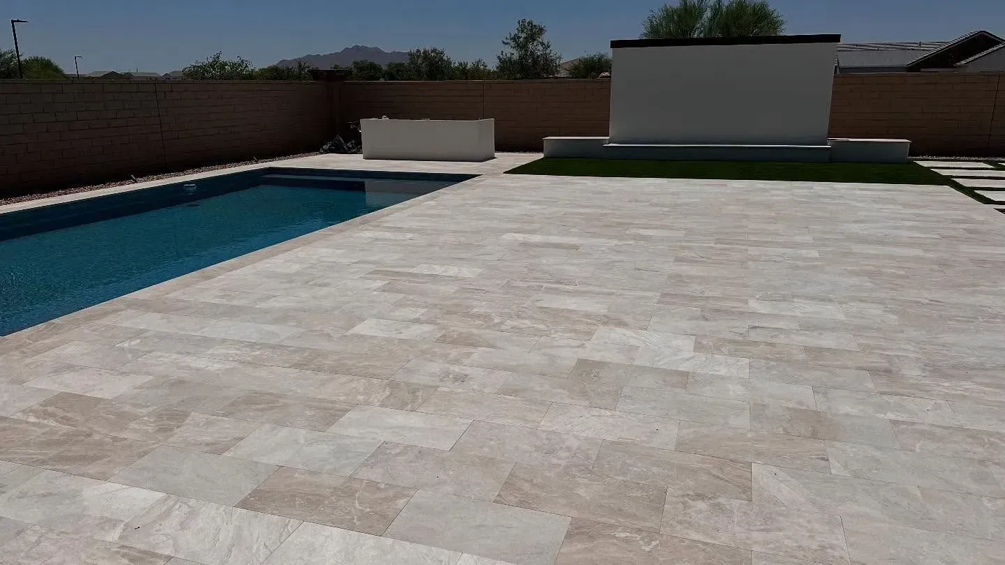 Pool with light stone patio, white wall, brown fence, and blue water.