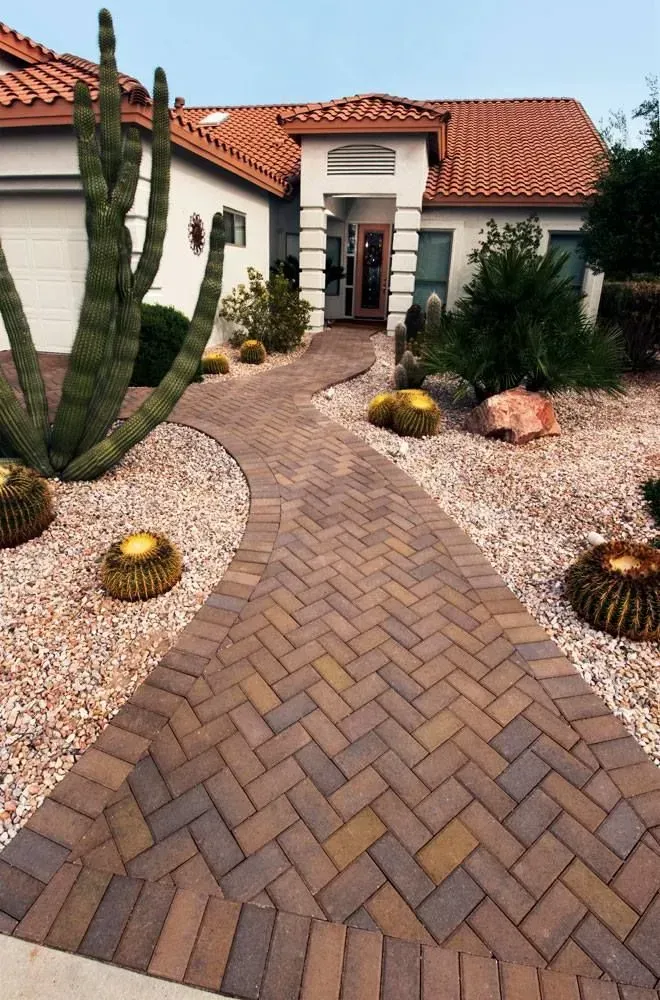 Brick pathway leading to a house with a red tile roof, surrounded by cacti and desert landscaping.