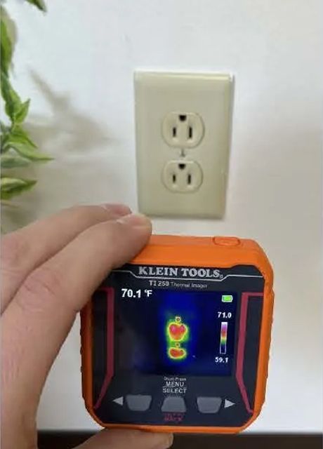 A person is holding a Klein Tools device in front of an outlet