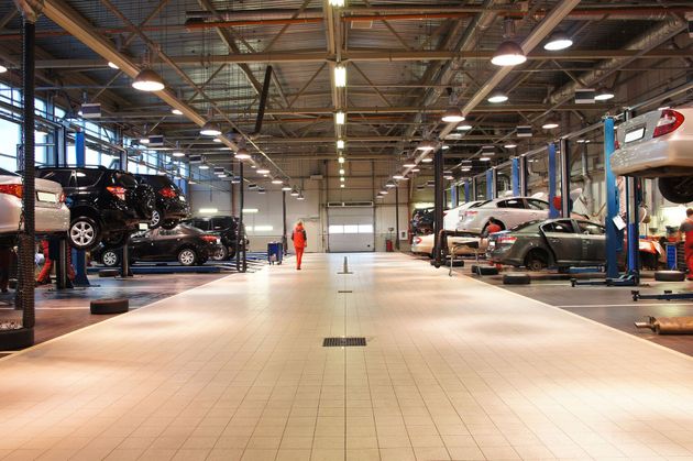 A bright, spacious car repair shop with multiple vehicles on lifts along the sides and an open center aisle.