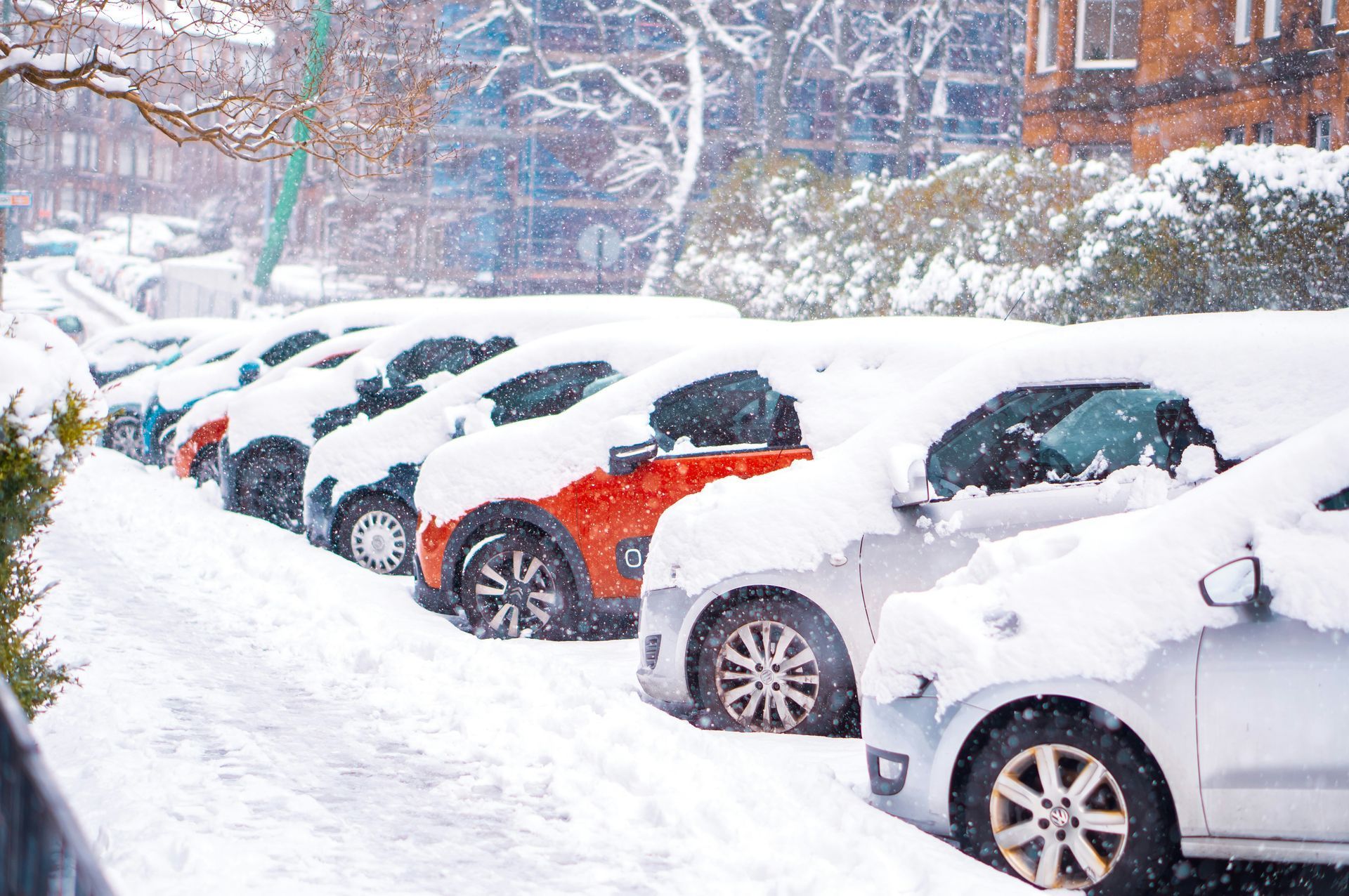 A row of cars parked on a street covered in deep snow during a winter day.