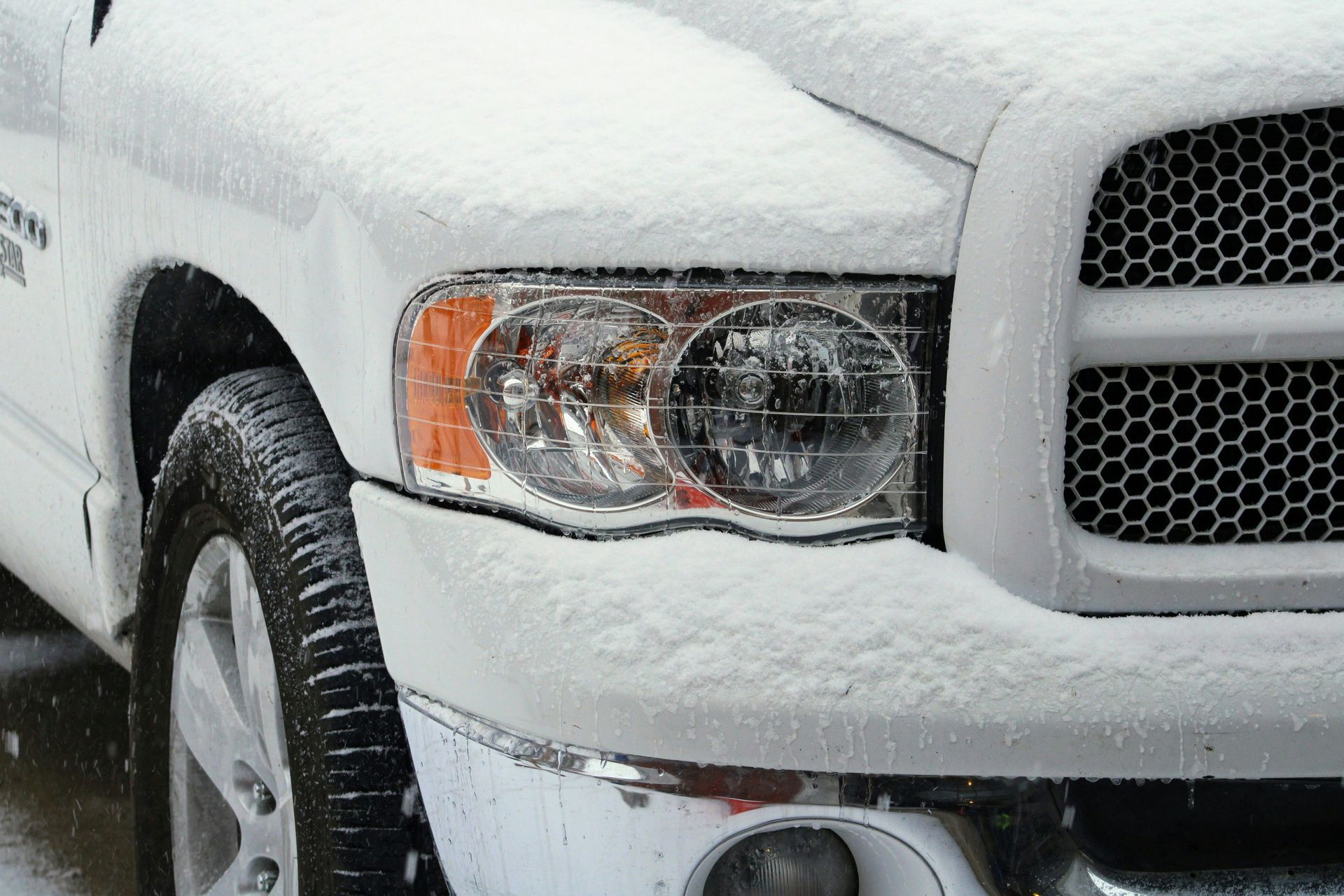 A close-up view of the front end of a white pickup truck partially covered in a light dusting of snow.