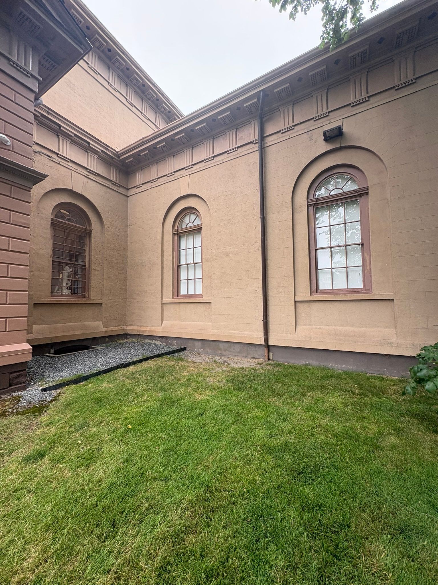 Courtyard with beige stucco walls, arched windows, and a patch of green grass under an overcast sky