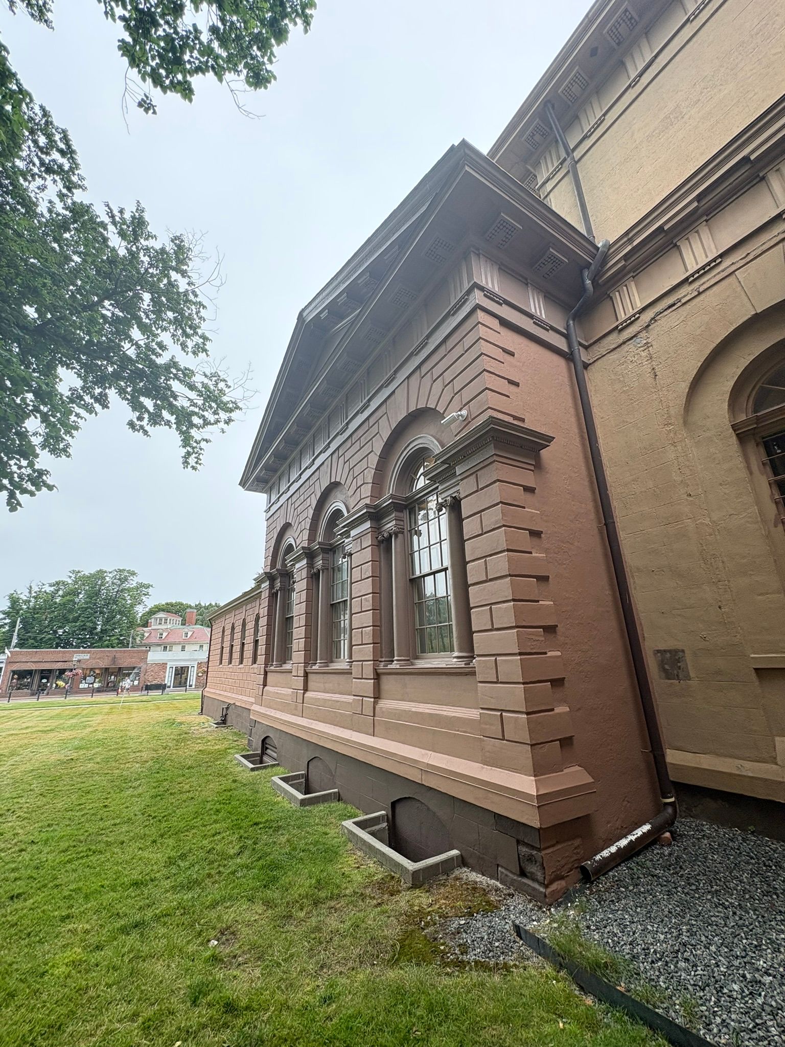 Side view of a historic brick building with arched windows beside a grassy lawn and trees