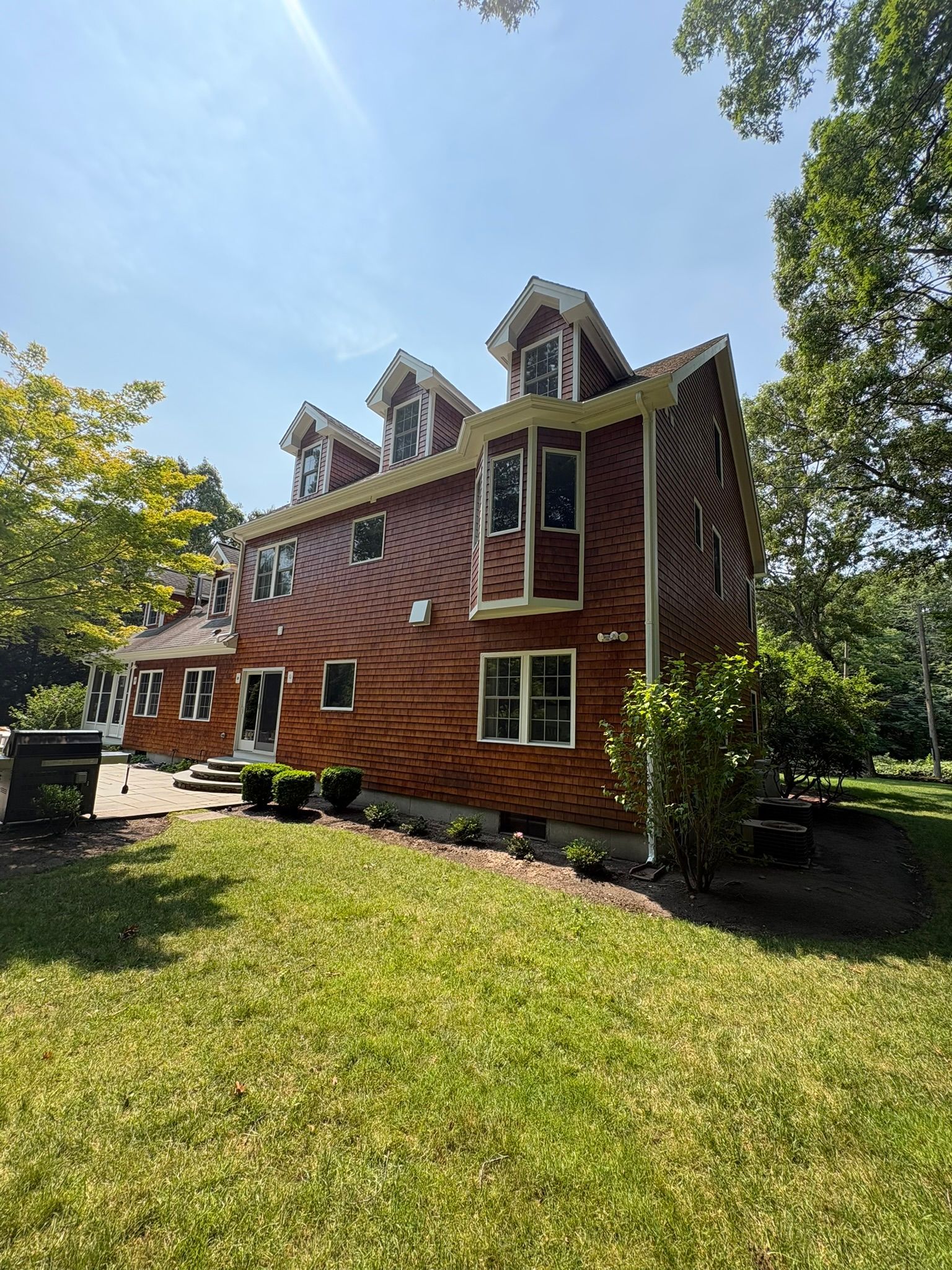 Red brick house with white trim and dormer windows on a sunny day, surrounded by green lawn and trees