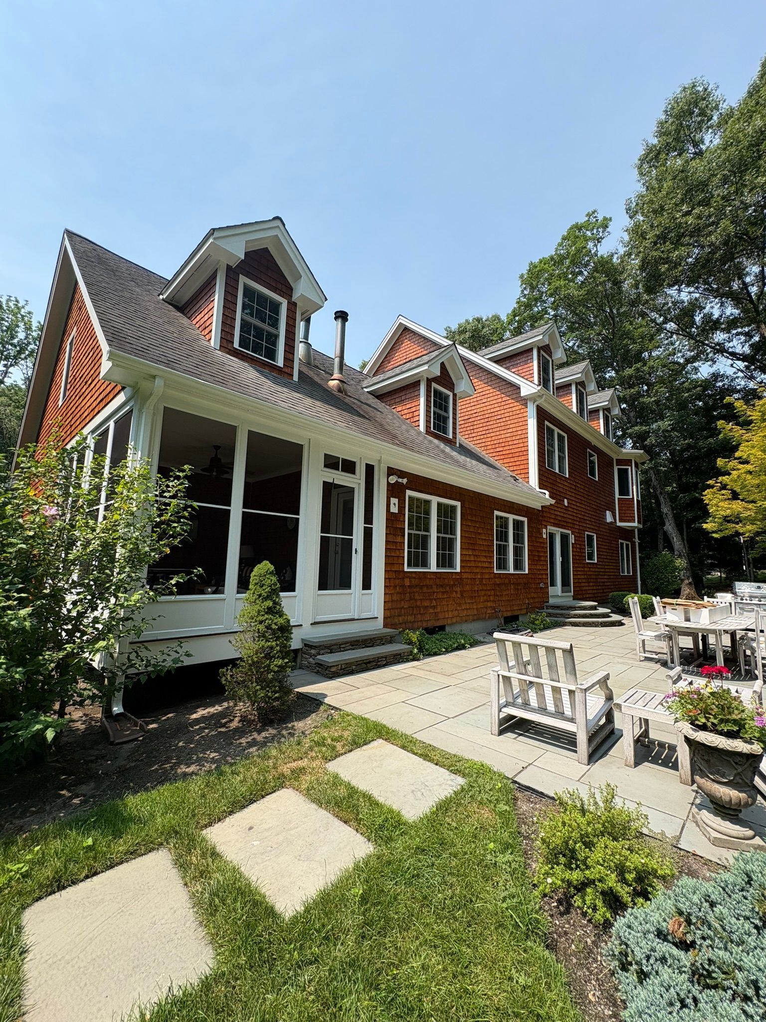 Brick house with red roof and white trim, viewed from a sunny garden patio with stepping stones.