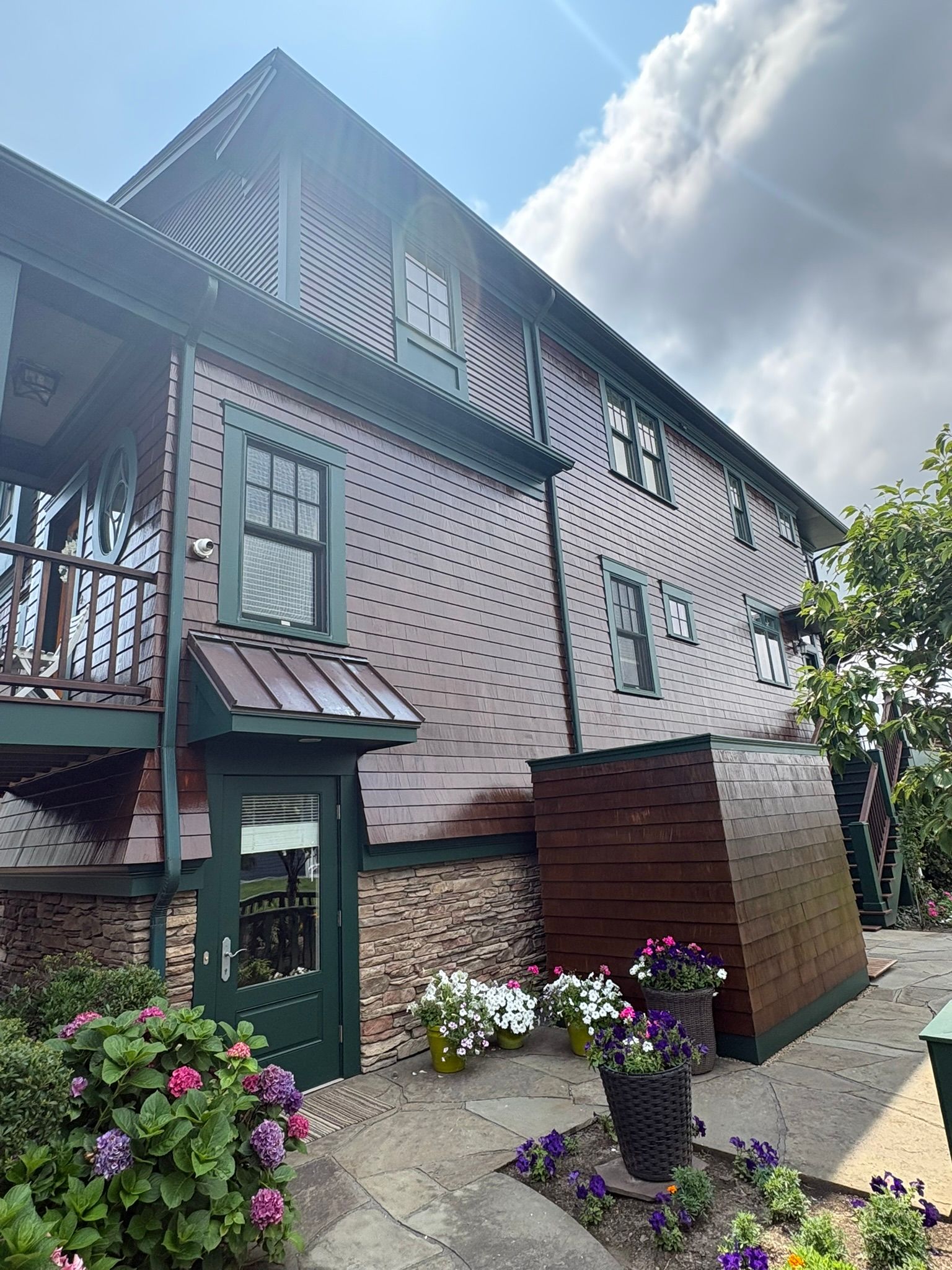 Tall half-timbered house with a green door, flower beds, and a cloudy sky