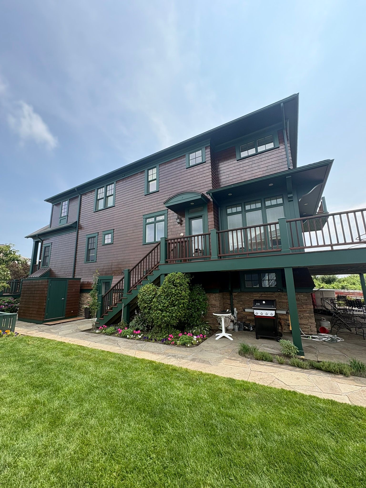 Two-story pink house with a deck, stairs, and green lawn under a blue sky